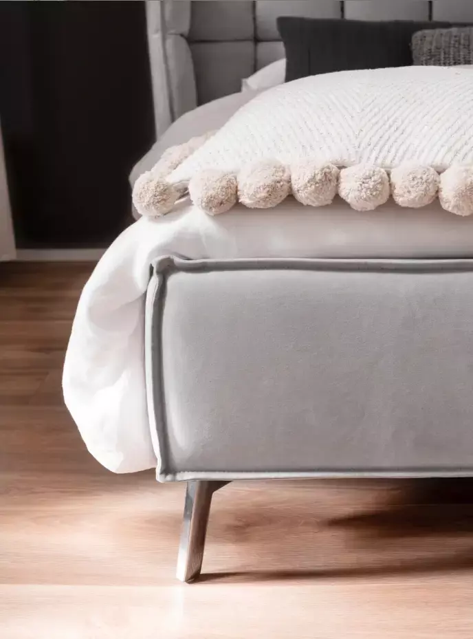 Nahaufnahme eines grauen Bettes mit weißer Bettwäsche, cremefarbener Chevron-Decke mit Bommeln