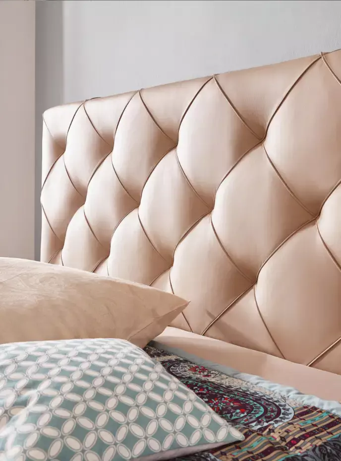 Beiges tuftiertes Bett mit beigen Kissen, türkisem Musterkissen und bunter Paisley-Decke.